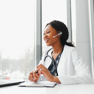 African American woman doctor working at her office online using portable inormation device. Telemedicine services. Primary care consultations, psychotherapy, emergency services.