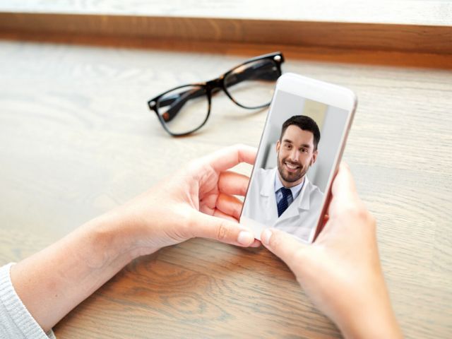 medicine, healthcare and technology concept - hands of woman having video call or online consultation with doctor on smartphone