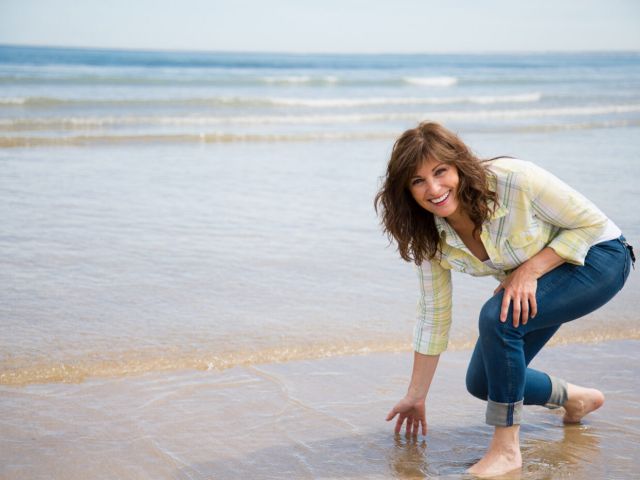Beautiful and funny middle aged woman splashing water with hand on the seashore