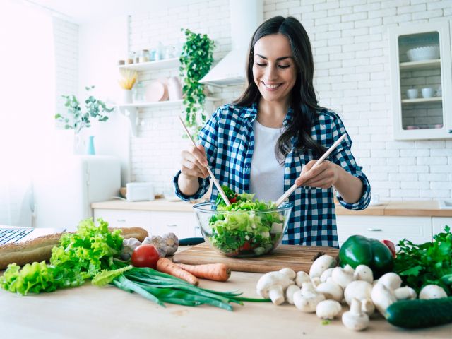 Beautiful young woman is preparing vegetable salad in the kitchen. Healthy Food. Vegan Salad. Diet. Dieting Concept. Healthy Lifestyle. Cooking At Home. Prepare Food. Cutting ingredients on table