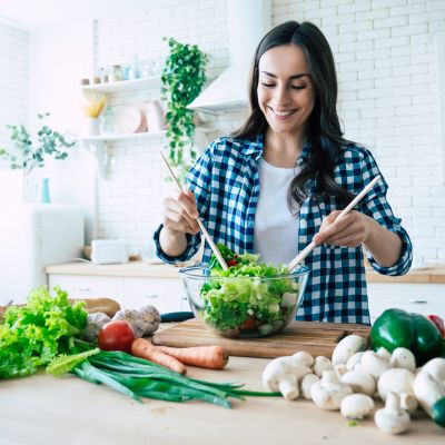 Beautiful young woman is preparing vegetable salad in the kitchen. Healthy Food. Vegan Salad. Diet. Dieting Concept. Healthy Lifestyle. Cooking At Home. Prepare Food. Cutting ingredients on table