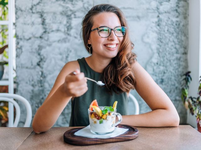 Young cheerful woman eating fruit salad.