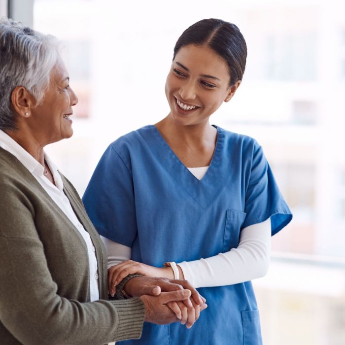 Support, caregiver with senior woman and holding hands for care indoors. Retirement, consulting and professional female nurse with elderly person smiling together for healthcare at nursing home