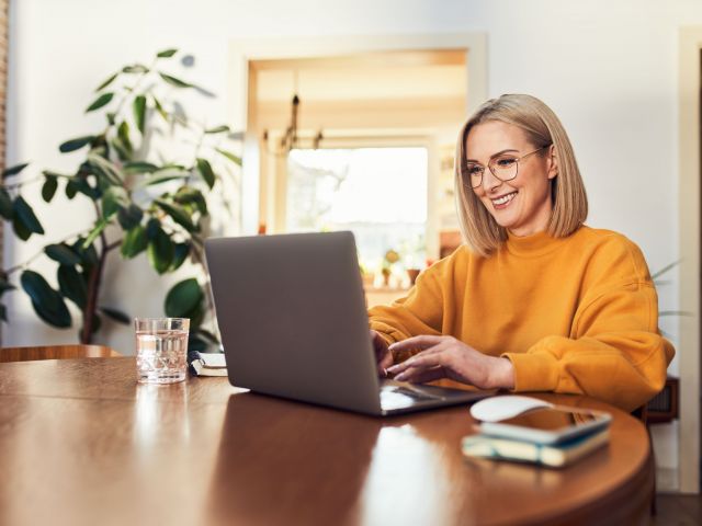 Happy mature woman using laptop while working remotely from home in living room