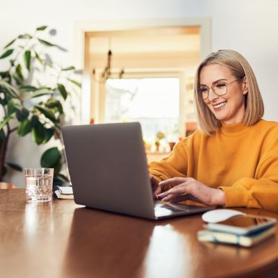 Happy mature woman using laptop while working remotely from home in living room