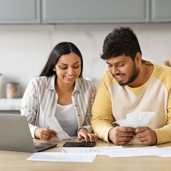 Smiling indian couple holding papers, calculating domestic bills, kitchen interior