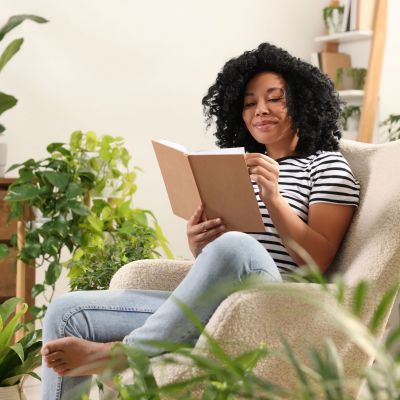 Relaxing atmosphere. Woman enjoying reading book near houseplants at home