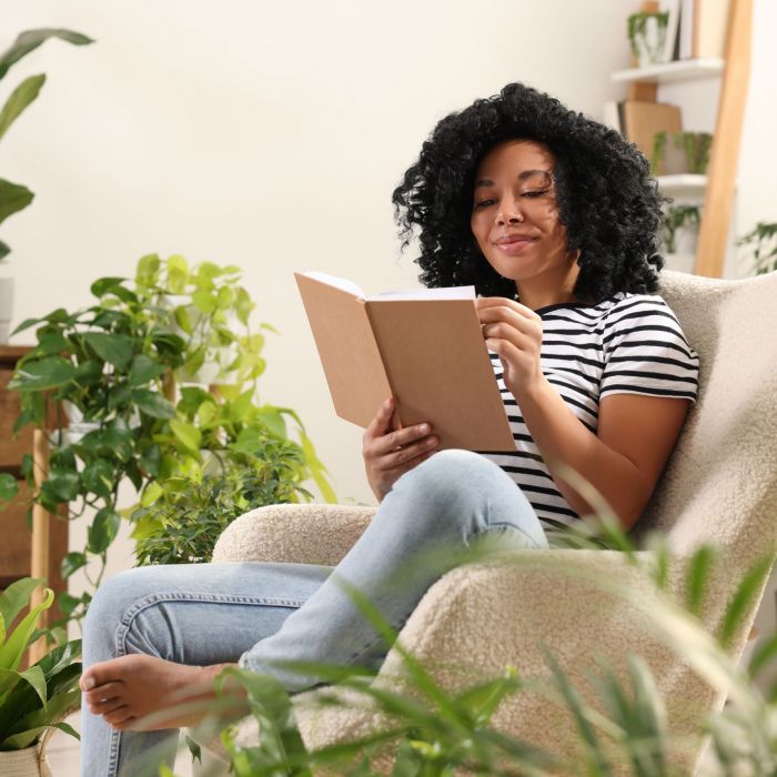 Relaxing atmosphere. Woman enjoying reading book near houseplants at home